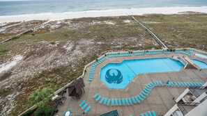 Un espace piscine au design original, entouré d’une terrasse agrémentée de chaises longues, avec une vue sur la plage en arrière-plan.