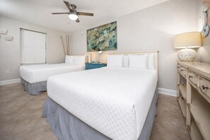 Ein Schlafzimmer mit zwei Betten, einem Deckenventilator, einem Gemälde, einer Nachttischlampe und einem Schminktisch.