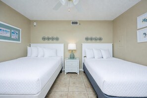 Ein Hotelzimmer mit zwei Betten, einem Nachttisch mit Lampe, Wandbildern und einem Deckenventilator.
