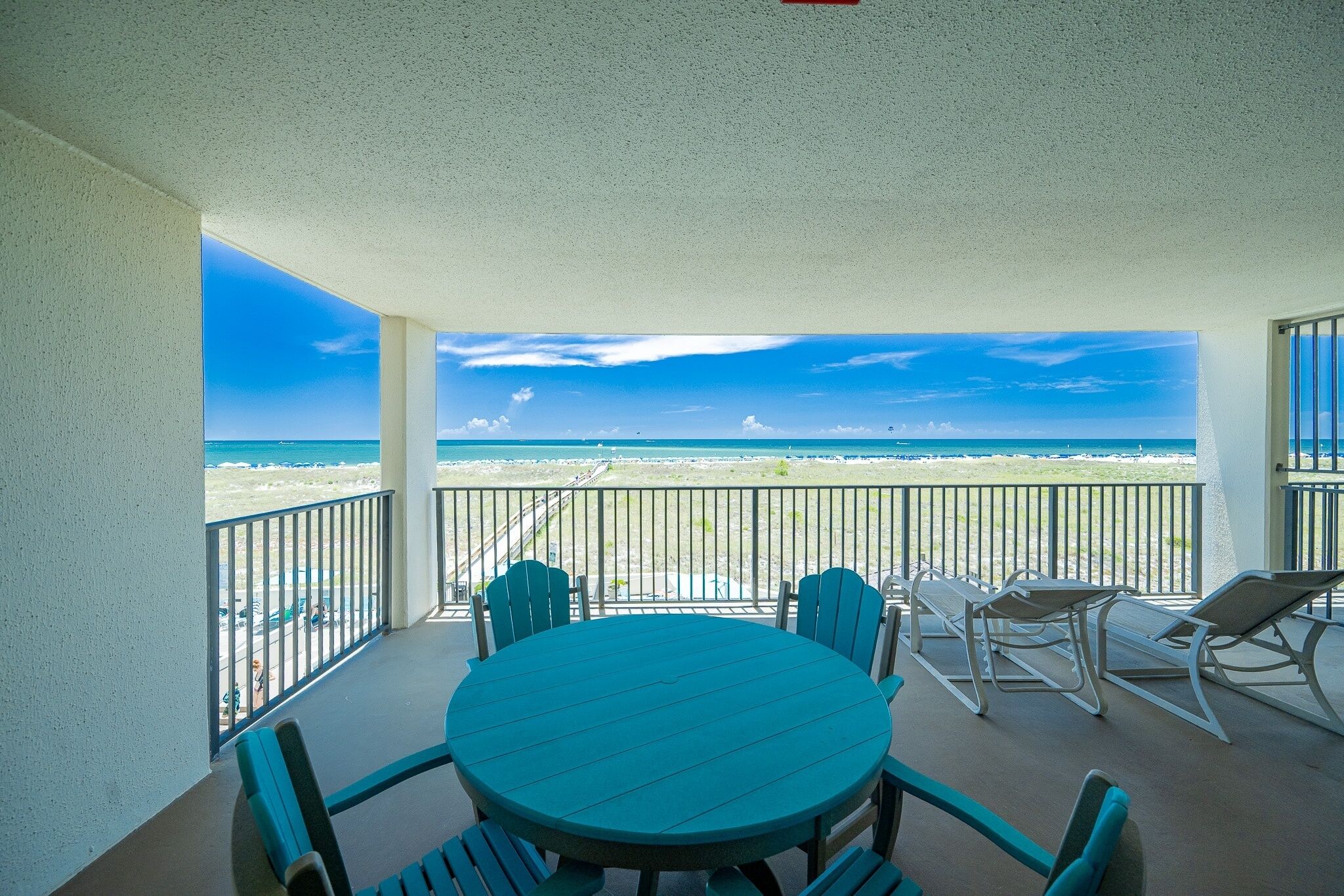 A balcony with a view of the beach, a round table, and four chairs.