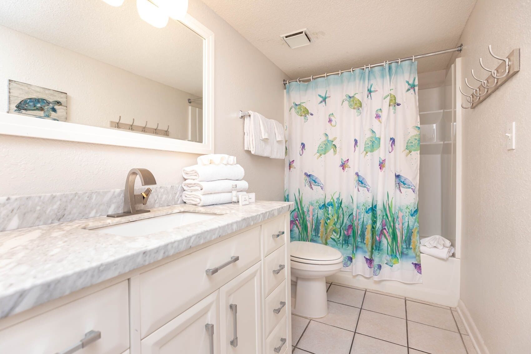 Une salle de bain avec un comptoir en marbre, des toilettes blanches, un rideau de douche orné de motifs marins et un porte-serviettes.