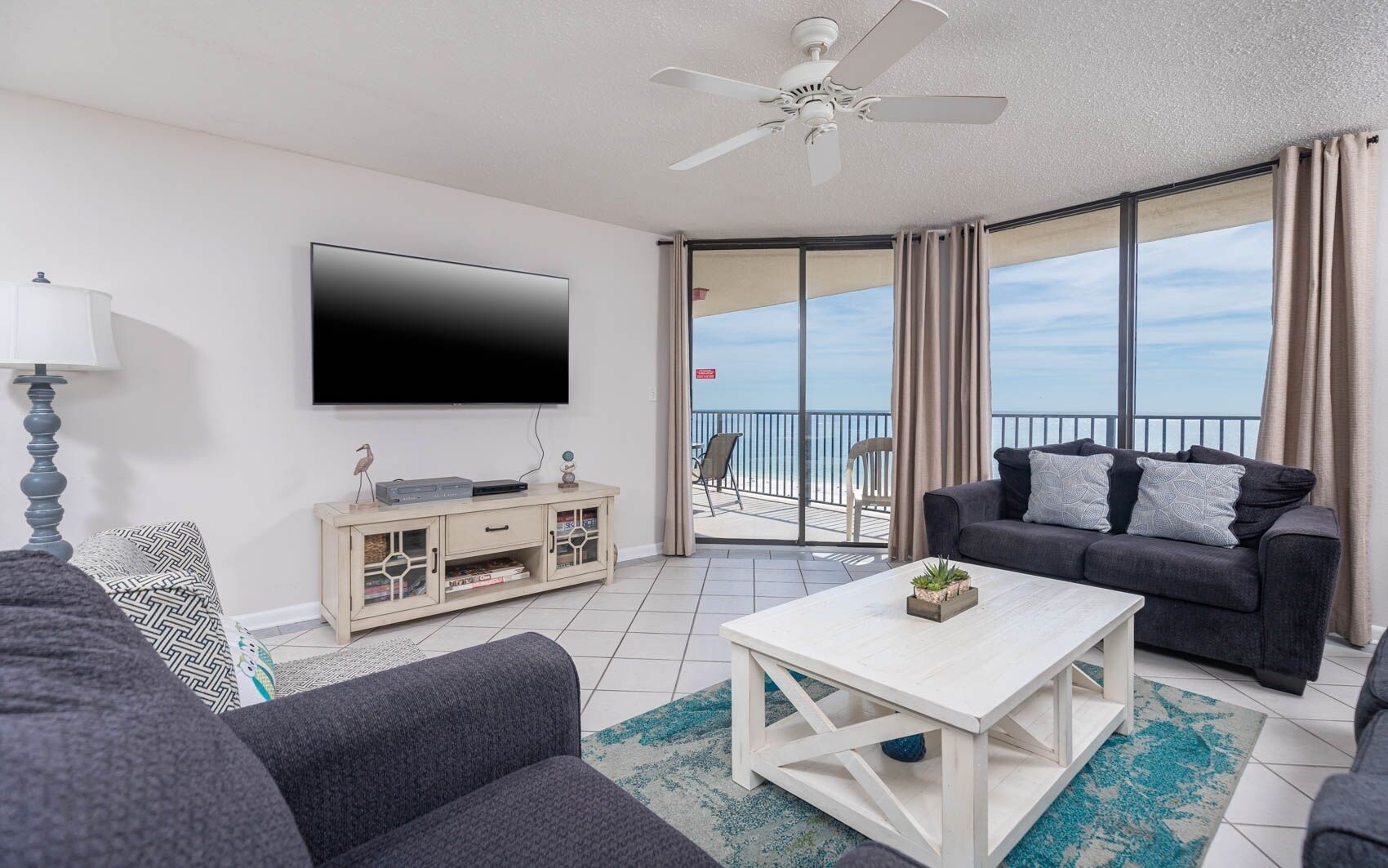 A modern living room with a flat-screen TV, a sofa, a coffee table, and a balcony with a view.