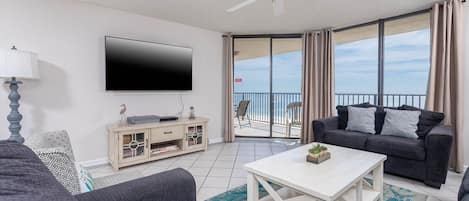 A modern living room with a flat-screen TV, a sofa, a coffee table, and a balcony with a view.