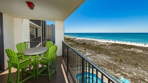 Un balcon avec une table et des chaises, donnant sur une plage avec une piscine.