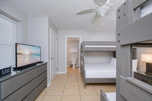 Une chambre d’hôtel équipée d’une télévision, de lits superposés, d’un ventilateur de plafond et d’une salle de bain avec des toilettes et un lavabo.