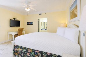 A hotel room with a bed, a desk, a television, a ceiling fan, and a painting on the wall. - Phoenix Viii 8606 3 Bedroom Condo (Orange Beach)