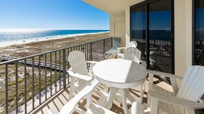 A balcony with white chairs and a table, overlooking a beach and ocean. - Phoenix Viii 8606 3 Bedroom Condo (Orange Beach)