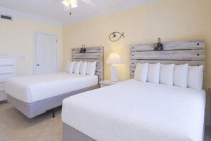 A hotel room with two beds, a nightstand with a lamp, a wall clock, and a door. - Phoenix Viii 8606 3 Bedroom Condo (Orange Beach)