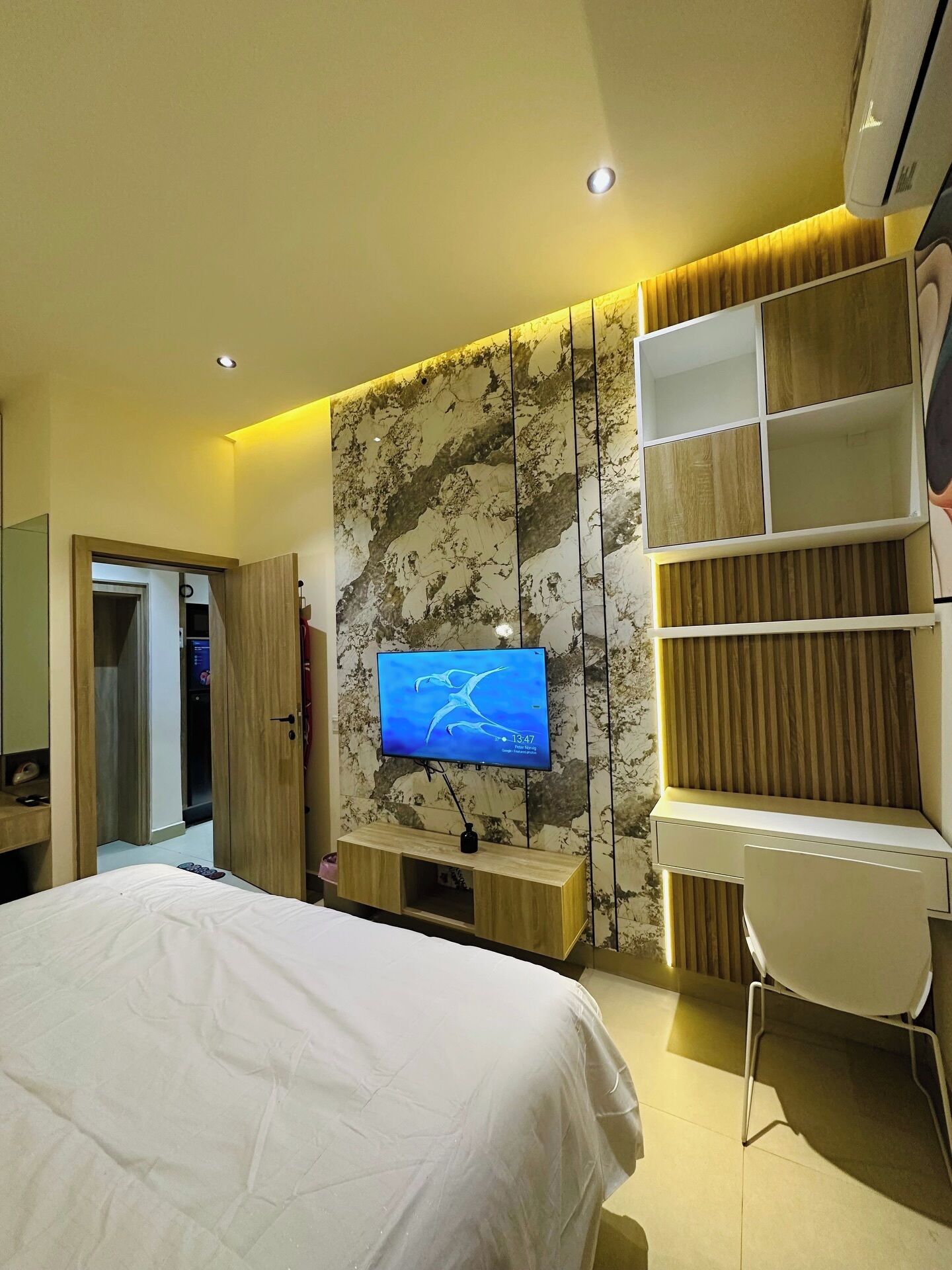 Un dormitorio con cama, televisor en la pared, escritorio y silla.
