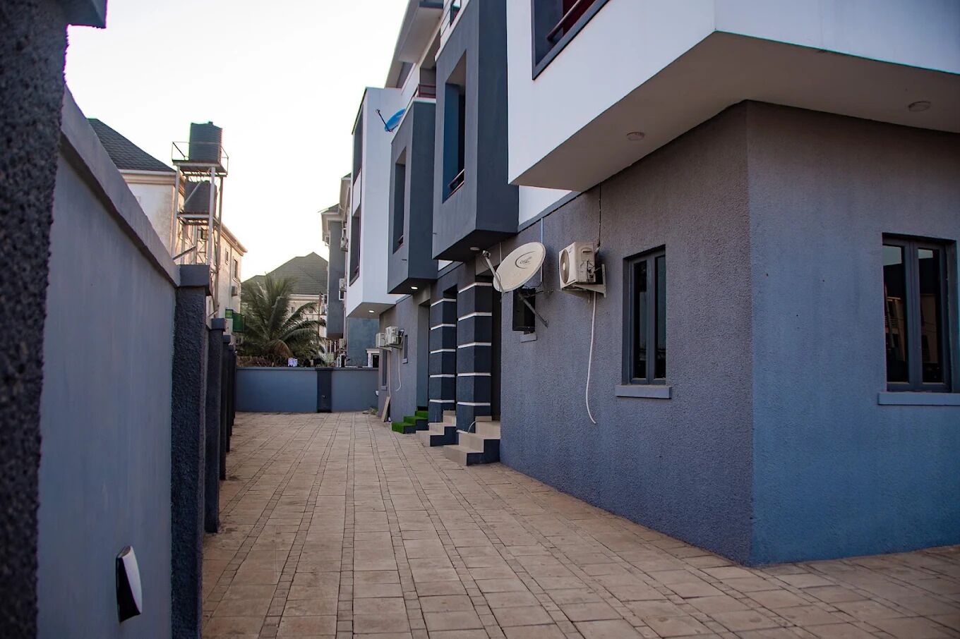 A modern residential building with a paved courtyard, satellite dishes, and a visible staircase leading to the entrance.
