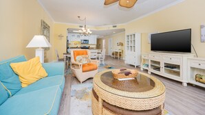 A living room with a blue sofa, a round wicker coffee table, and a flat-screen TV. - Phoenix Vii 71205 3 Bedroom Condo (Orange Beach)