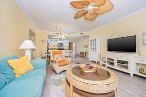 A living room with a blue sofa, a round wicker coffee table, and a flat-screen TV. - Phoenix Vii 71205 3 Bedroom Condo (Orange Beach)