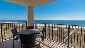 Ein Balkon mit Tisch und Stühlen mit Blick auf einen Strand und den Ozean.