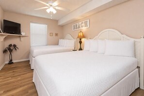 Ein Schlafzimmer mit zwei Betten, einem Deckenventilator, einem Fernseher und einem Wandschild mit der Aufschrift 'BEACH'.