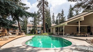 Zona de piscina amb gandules, un espai d'estar cobert i arbres alts al fons.