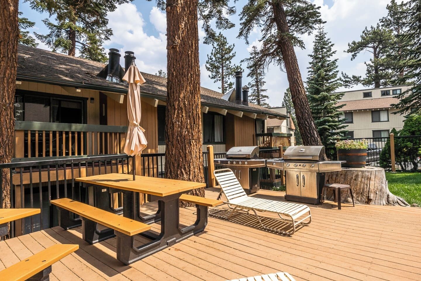 Une terrasse avec des tables et des chaises en bois, un barbecue et un fauteuil de relaxation.