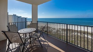 A balcony with a table and chairs, overlooking a beach and ocean. - Phoenix Vii 71213 2 Bedroom Condo (Orange Beach)