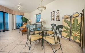 A dining area with a glass table, metal chairs, a potted plant, and artwork on the walls. - Phoenix Vii 71213 2 Bedroom Condo (Orange Beach)