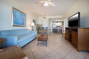 A living room with a sofa, a coffee table, a TV, and a dining area with chairs and a table. - Phoenix Vii 71213 2 Bedroom Condo (Orange Beach)