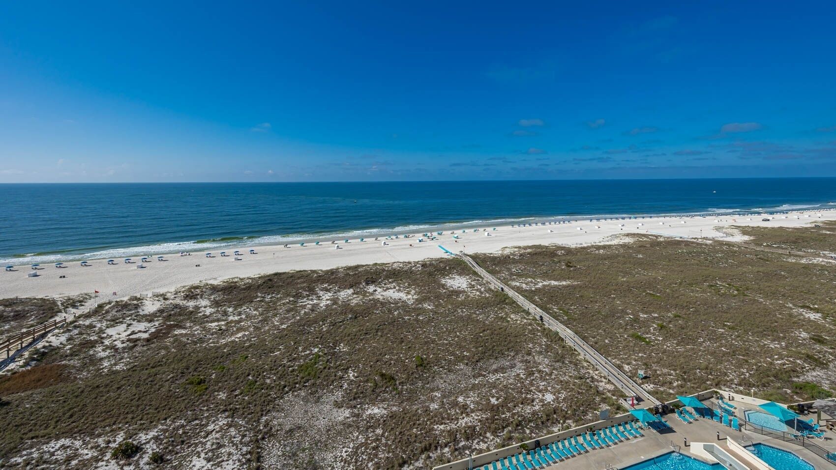 Un resort sulla spiaggia con piscina, lettini e una passeggiata sul mare.