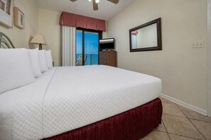 A hotel room with a large bed, a television, a mirror, and a balcony with a view. - Phoenix Vii 71213 2 Bedroom Condo (Orange Beach)