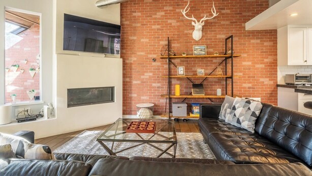 A living room with a brick wall, a mounted deer head, a glass coffee table, a leather sofa, and a fireplace. - Summer Retreat in Style! Newly Renovated 2BR/3BA (Mammoth Lakes)