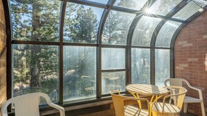 A conservatory with a glass ceiling, wooden walls, and a view of trees. Inside, there is a round table with chairs. - Summer Retreat in Style! Newly Renovated 2BR/3BA (Mammoth Lakes)