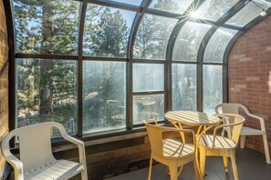 Ein Wintergarten mit Glasdach, Holzvertäfelung und Blick auf Bäume. Darin steht ein runder Tisch mit Stühlen.