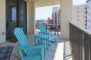 A balcony with turquoise chairs and a table, overlooking a cityscape with buildings. - Phoenix Viii 81106 3 Bedroom Condo (Orange Beach)