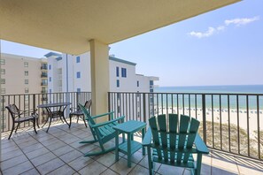 A balcony with a table and chairs, a view of the beach, and a building in the background. - Phoenix Viii 81106 3 Bedroom Condo (Orange Beach)