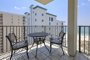 Ein Balkon mit Tisch und zwei Stühlen mit Blick auf einen Strand.