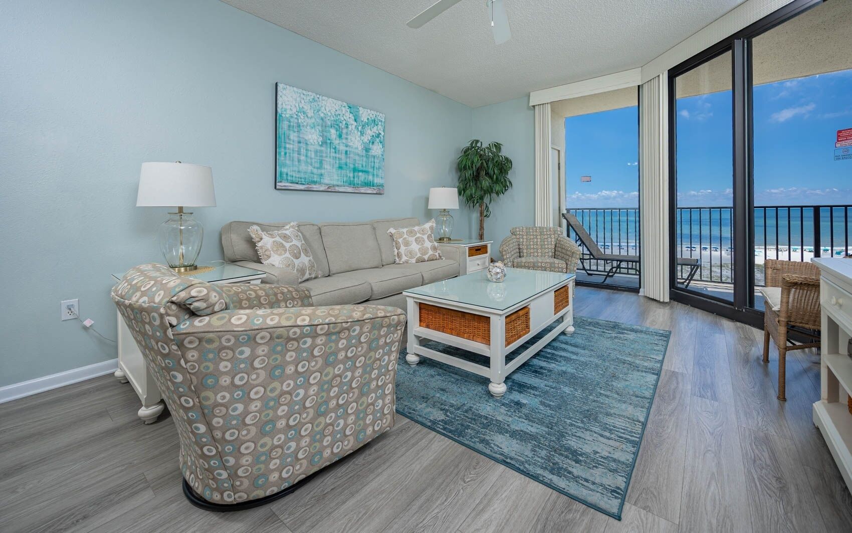 A living room with a sofa, armchair, coffee table, and a view of the ocean through large windows.
