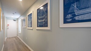 En hall med inramade arkitektoniska ritningar på väggen, ett trägolv och en vit dörr längst ner.