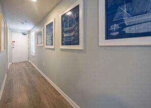 Ein Korridor mit gerahmten architektonischen Zeichnungen an der Wand, einem Holzboden und einer weißen Tür am Ende.