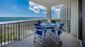 Ein Balkon mit Tisch und Stühlen, mit Blick auf einen Strand und ein Hochhaus.