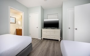 Ein Hotelzimmer mit zwei Betten, einem Fernseher auf einem Schminktisch und einer Tür zu einem Badezimmer.