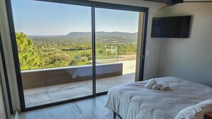 Une chambre à coucher avec un lit, une télévision et un balcon donnant sur la campagne.