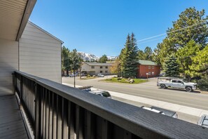 A view from a balcony overlooking a street with buildings, a truck, and a mountain in the background. - Stylish in Central Mammoth! 2 Bed / 2 Bath + Loft (Mammoth Lakes)