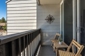 A wooden deck with a metal compass wall decoration, a sliding glass door, and a small table with chairs. - Modern Cabin Charm! 2BR/2BA in Central Mammoth! (Mammoth Lakes)