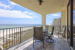 Ein Balkon mit Blick auf den Strand und den Ozean, möbliert mit Korbstühlen und einem Tisch.