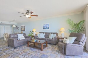 A living room with a ceiling fan, two sofas, a coffee table, and a dining area with chairs. - Phoenix Viii 81104 3 Bedroom Condo (Orange Beach)
