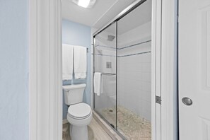 A bathroom with a toilet, a glass shower enclosure, and a white door. - Pointe Santo Unit C22 2 Bedroom Condo (Sanibel)