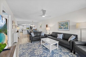 A modern living room with a sofa set, a coffee table, and a view of the kitchen and dining area. - Pointe Santo Unit C22 2 Bedroom Condo (Sanibel)