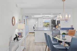 A modern kitchen with white cabinetry, a central island, and a dining area with a glass table and chairs. - Pointe Santo Unit C22 2 Bedroom Condo (Sanibel)