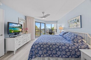 A bedroom with a large bed, a TV, a balcony with a view, and a ceiling fan. - Pointe Santo Unit C22 2 Bedroom Condo (Sanibel)