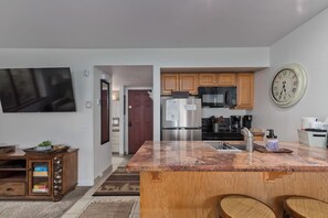 A modern kitchen with a granite countertop, stainless steel appliances, wooden cabinets, and a wall-mounted clock. - Less driving, More Skiing! Steps to Canyon Gondola (Mammoth Lakes)