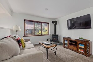 Ein Wohnzimmer mit einer Couch, einem Tisch, einem Fernseher, einem Kamin und einem Schrank.