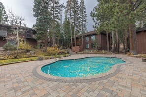 A swimming pool with a brick border, surrounded by trees and a building with a wooden exterior. - Less driving, More Skiing! Steps to Canyon Gondola (Mammoth Lakes)