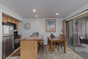 A compact kitchen with a central island, wooden cabinets, a stainless steel refrigerator, and a dining area with a table and chairs. - Less driving, More Skiing! Steps to Canyon Gondola (Mammoth Lakes)