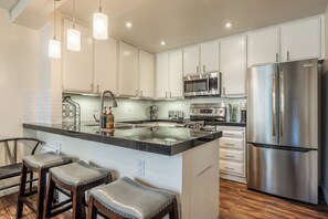 A modern kitchen with white cabinets, stainless steel appliances, a central island with stools, and pendant lighting. - Stunning Sunlit & Spacious-1BR/2BTH+Loft (Mammoth Lakes)